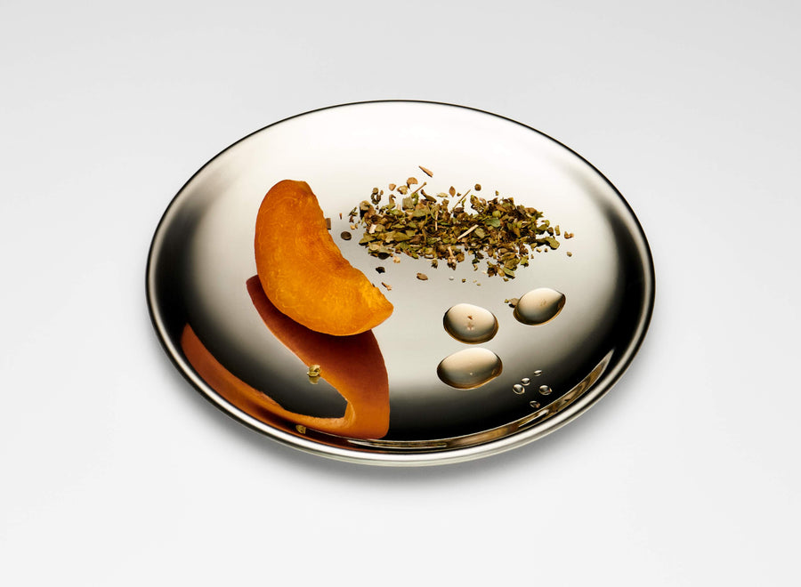 Slice of apricot, sprinkled zaatar, and juice drops on a silver mirror dish, with a white background.