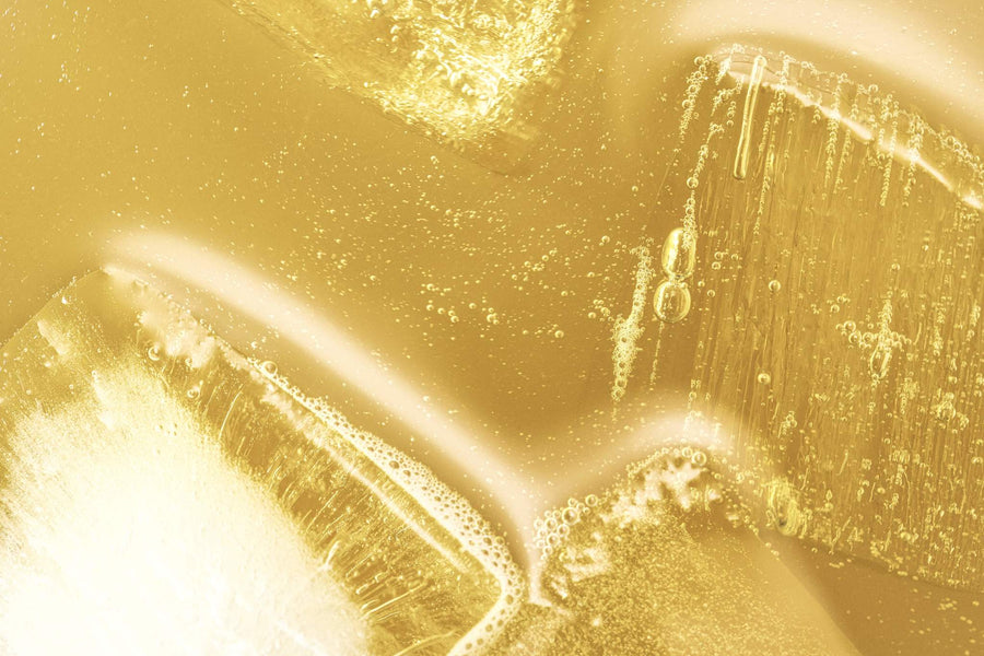 Abstract close-up of Pear & Anise: golden fizzy, sparkling liquid, with ice floating in warm, monochromatic color scheme. 