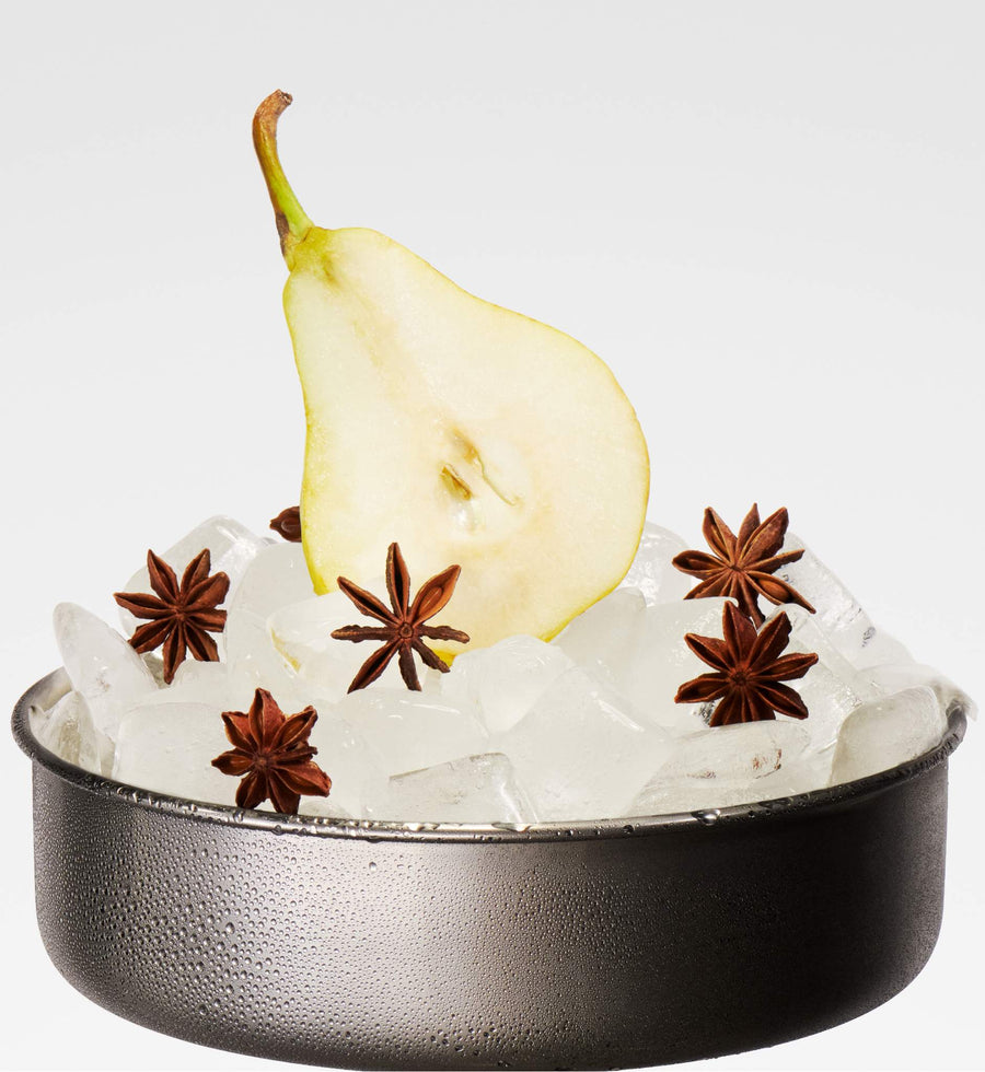 Ice bucket on pedestal with sliced pear and star anise placed on ice cubes against white background.