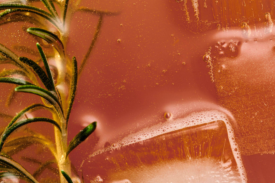 Close-up of a fizzy, amber-colored Douze Apricot & Za'atar drink with a floating rosemary sprig and ice.